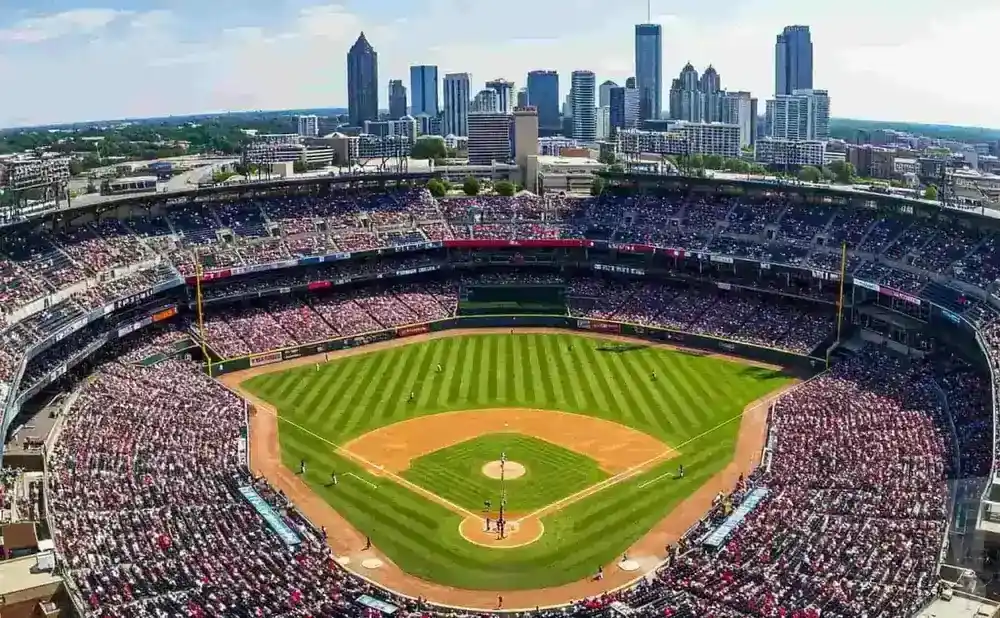 Aerial view of a baseball stadium filled with fans, with a cityscape in the background.