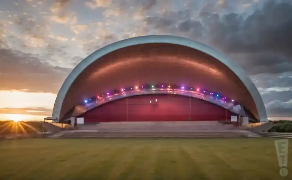 An outdoor amphitheater with a domed roof is lit with colorful lights at sunset.