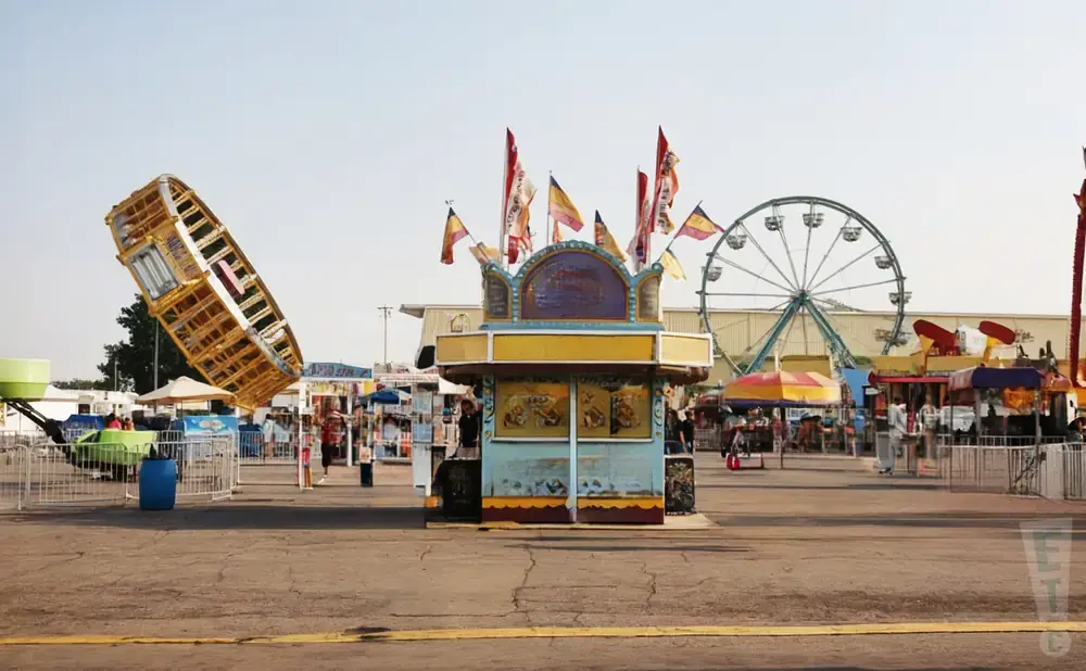 An amusement park with a Ferris wheel, rides, and food stalls under a clear sky.