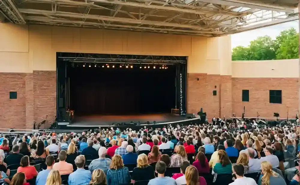 An outdoor amphitheater filled with a seated audience facing a stage with a dark curtain.