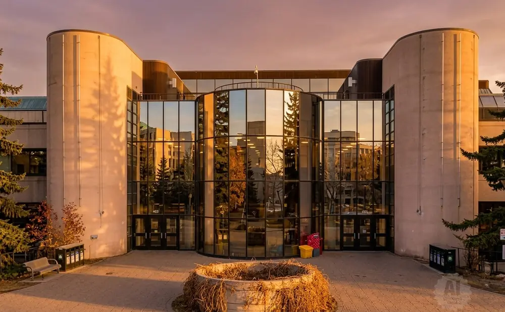 Golden hour sunset illuminates a modern building with large glass windows reflecting trees and sky.