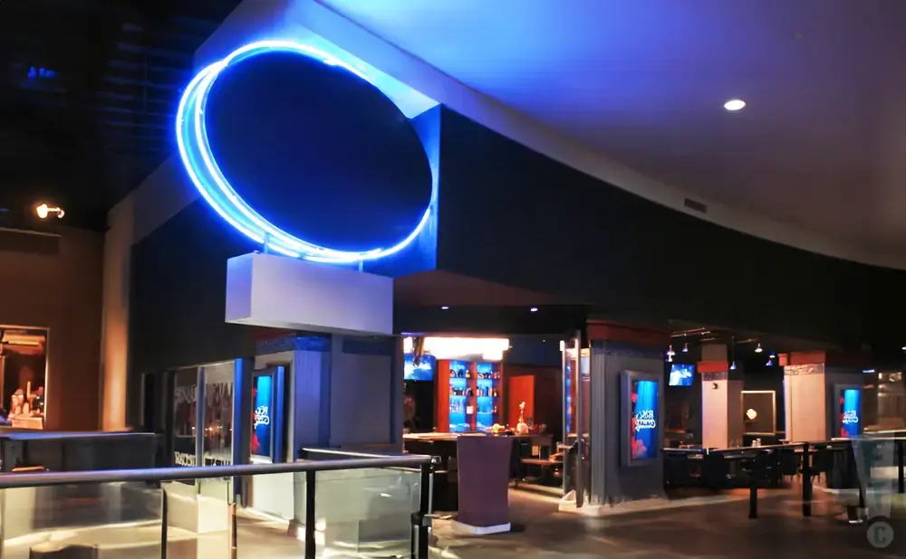 A large blue neon ring hangs above a bar area in a modern building.