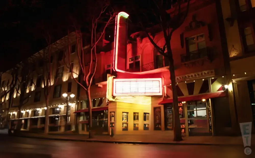 A vintage theater at night with a glowing marquee and neon lights.