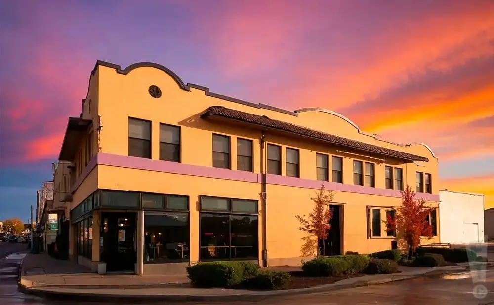 A yellow building with a pink stripe under a vibrant orange and purple sunset sky.