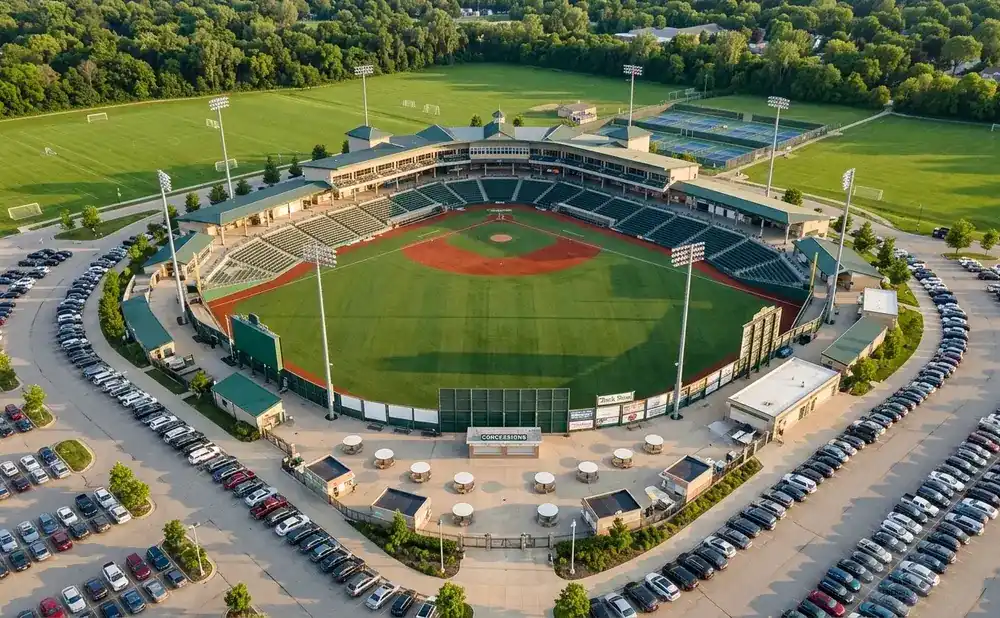 Aerial view of a baseball stadium, its field, grandstands, and surrounding parking lots filled with cars.
