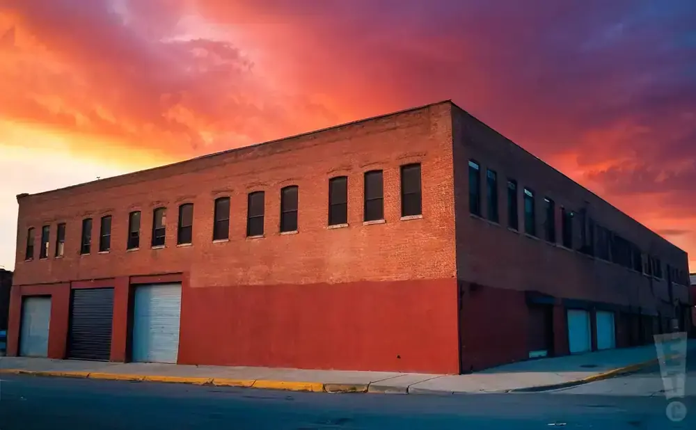 An old brick building with a red lower facade stands under a fiery sunset sky.