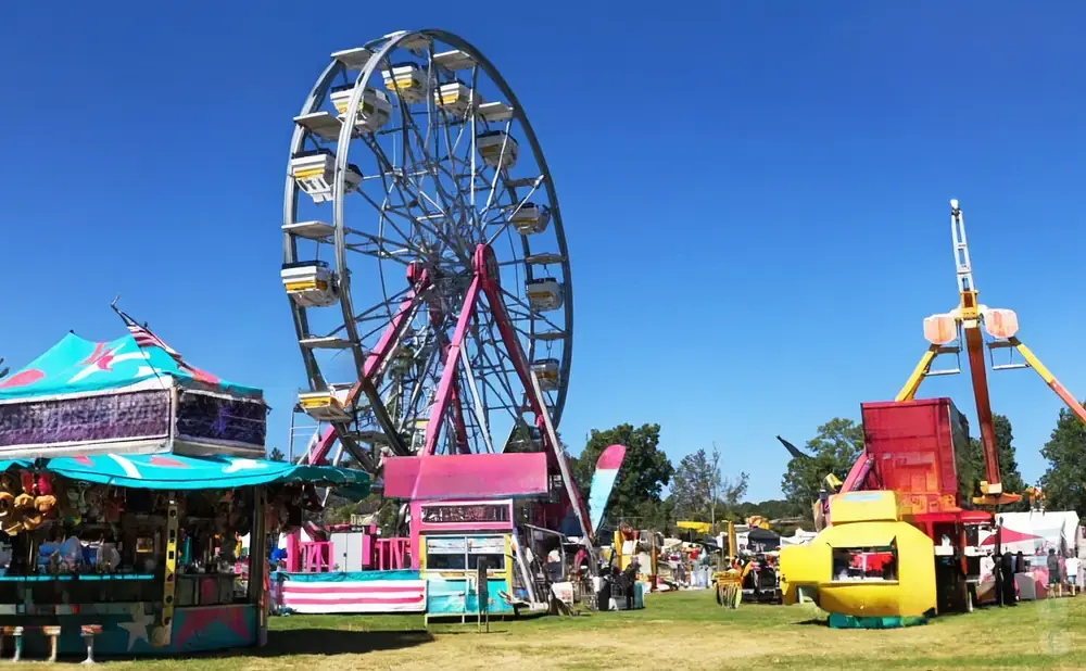 A carnival scene with a Ferris wheel, rides, and game booths under a clear blue sky.