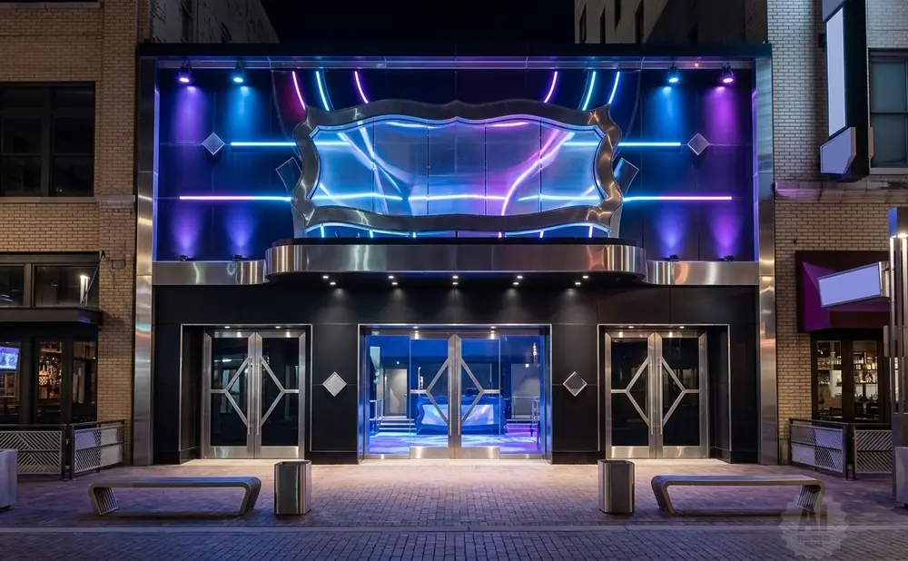 Exterior of a modern building at night, featuring colorful neon lights, glass doors, and benches.