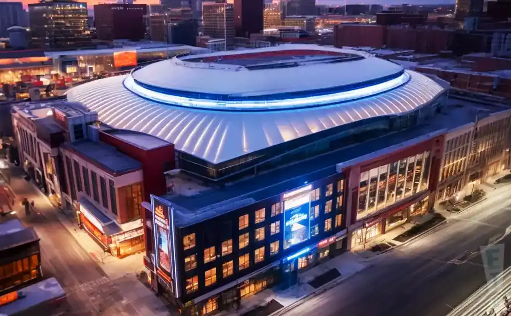 Aerial view of an illuminated domed stadium with surrounding buildings at dusk.