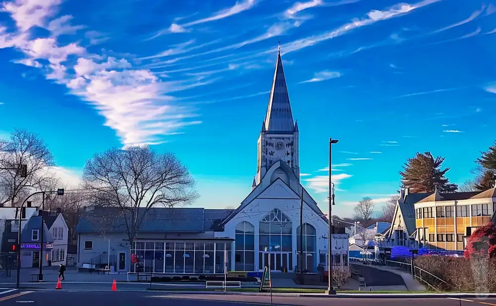 Church steeple against a bright blue sky with wispy clouds and bare trees.
