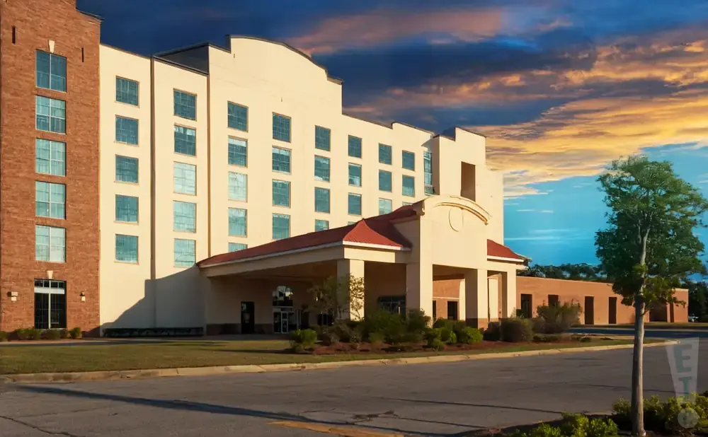 A hotel with a brick section and tan facade stands under a dramatic sunset sky.