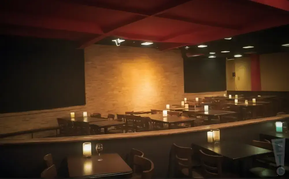 Empty tables with lit candles in a dimly lit restaurant or event space with a brick wall.