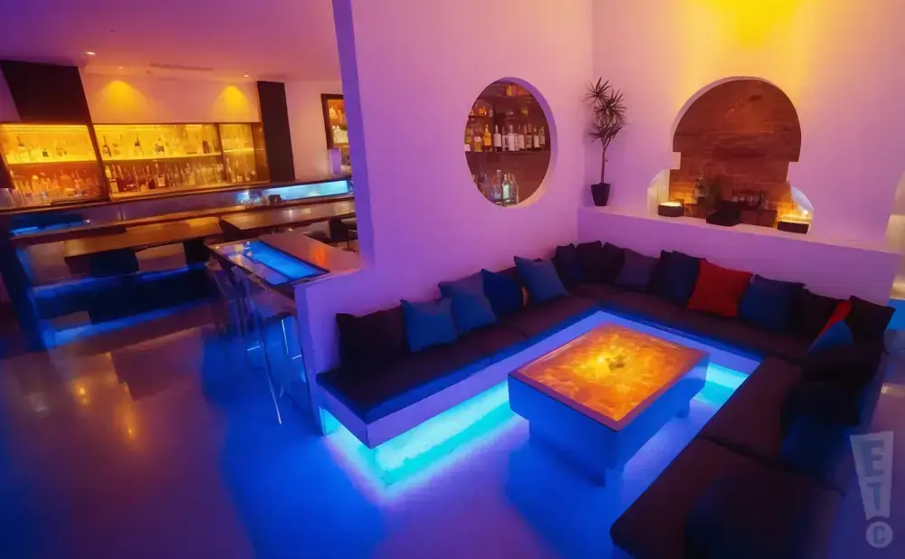 Modern lounge with U-shaped sofa, illuminated coffee table, and bar in background.