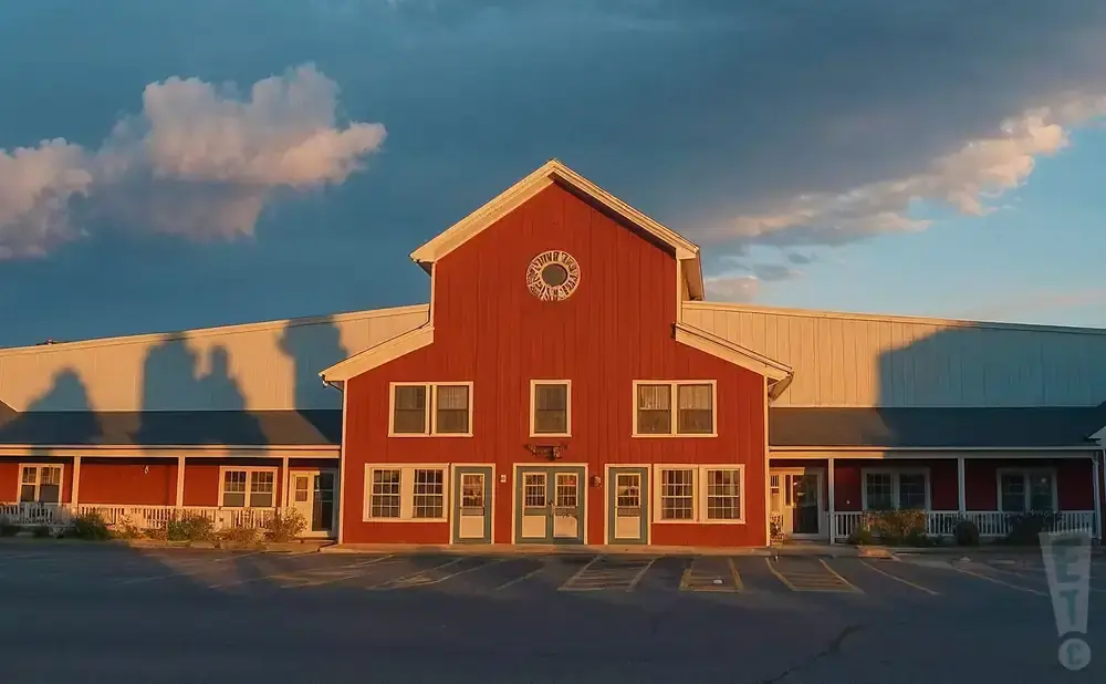 Red barn-style building with a long white wing, under a dramatic sky with pink clouds.