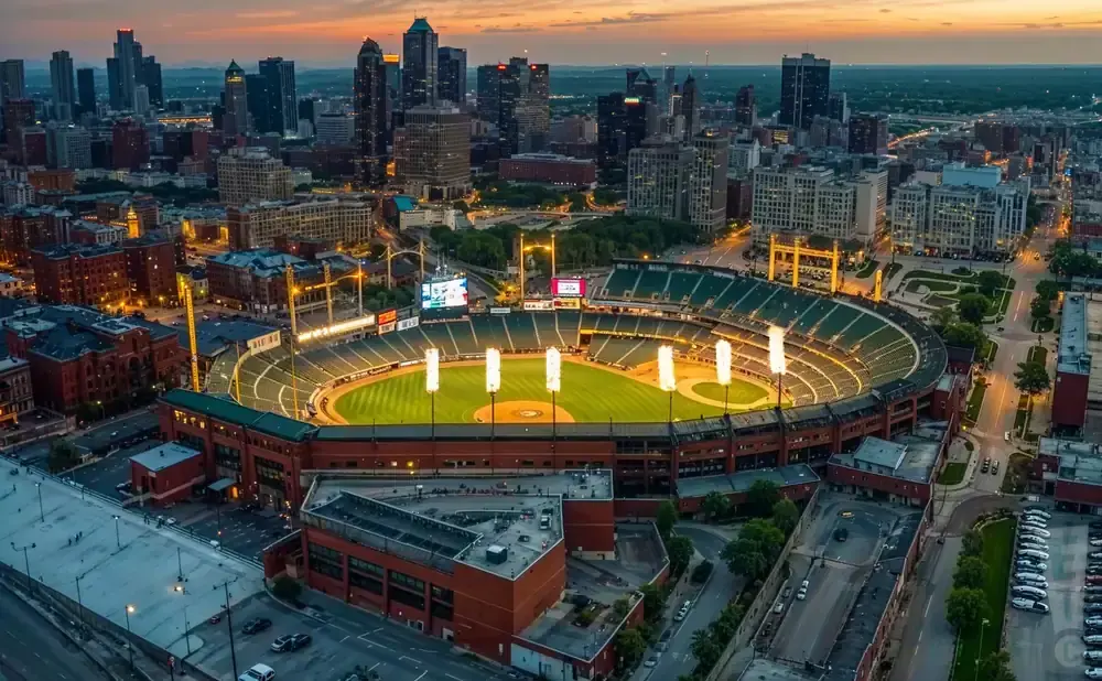 Aerial view of a baseball stadium at dusk, with city skyline in the background.