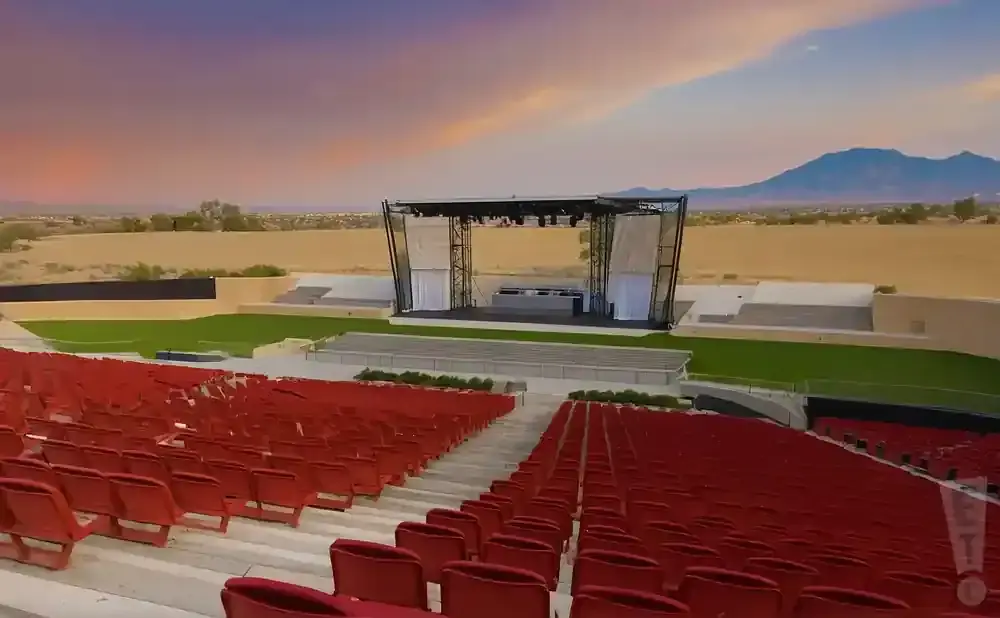 Outdoor amphitheater with red seats facing a stage. Mountains and a sunset sky are in the background.