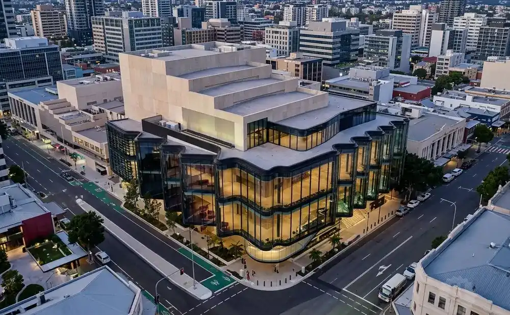 Aerial view of a modern building with curved glass facade and layered geometric upper structure, in a cityscape.