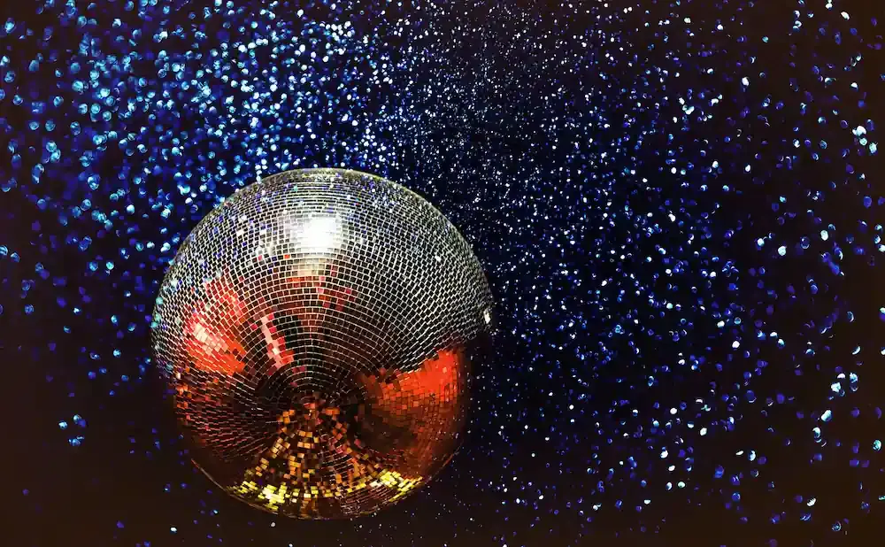 A disco ball reflects red and gold light against a dark background speckled with blue glitter.