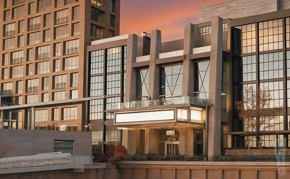 Modern buildings with large windows reflecting the sunset, and a lit marquee entrance.