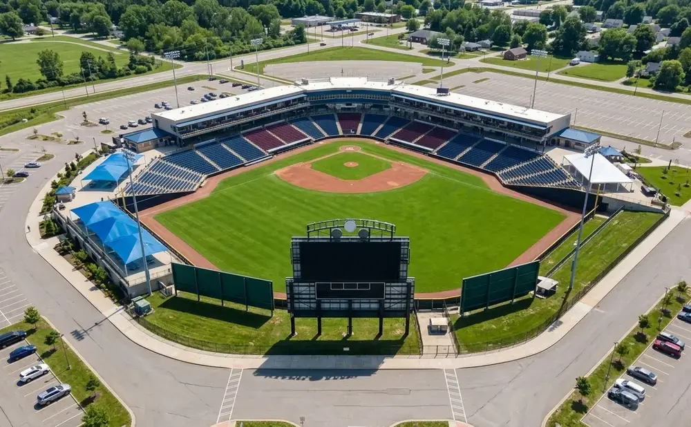 Aerial view of a baseball stadium with a green field, blue and red seats, and a large scoreboard.