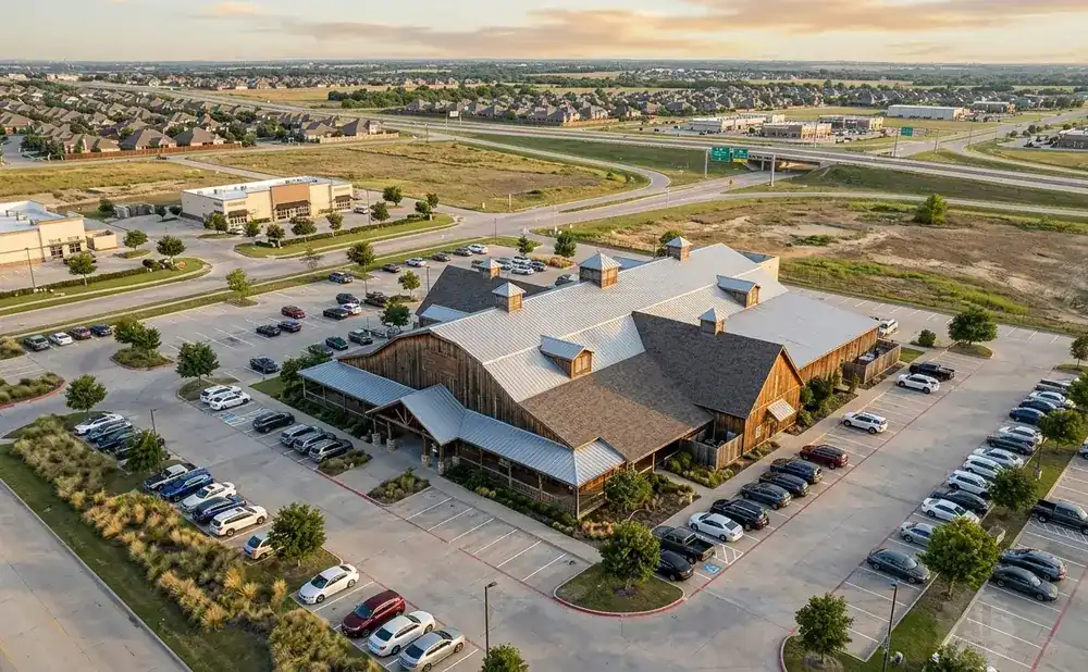 Aerial view of a large barn-style building with a parking lot full of cars.