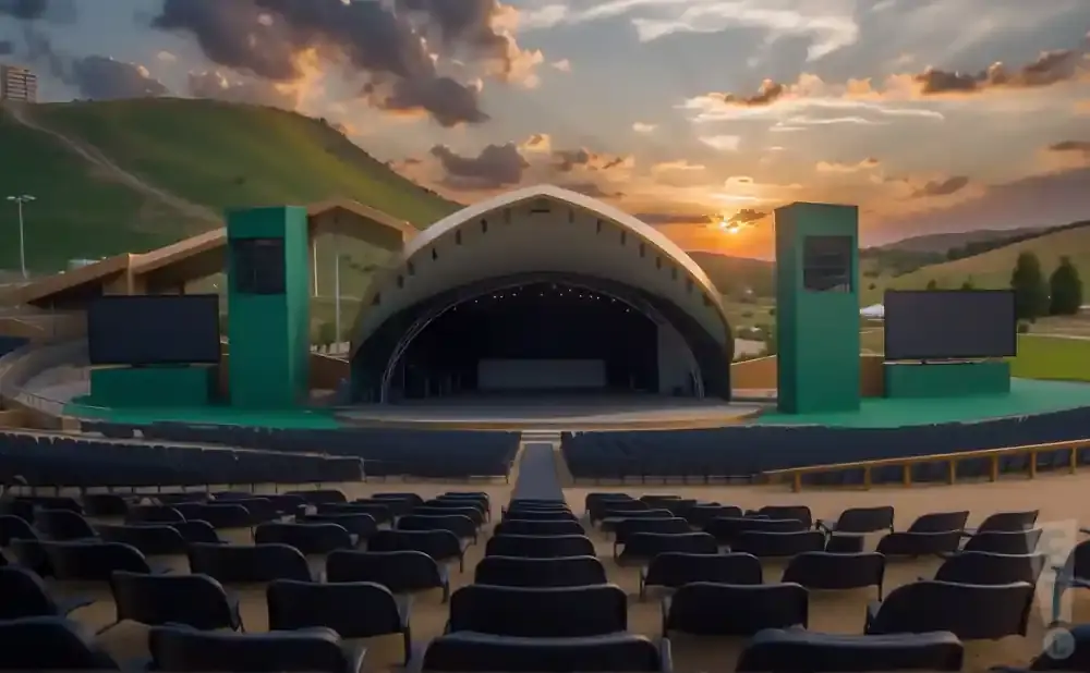An outdoor amphitheater with a stage and seating is shown at sunset.