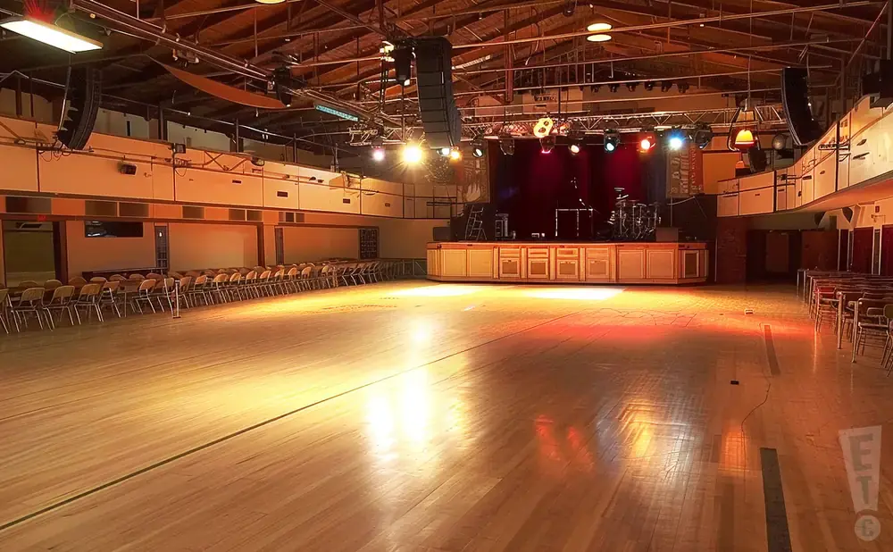 An empty ballroom with a stage, chairs, and wooden floors.