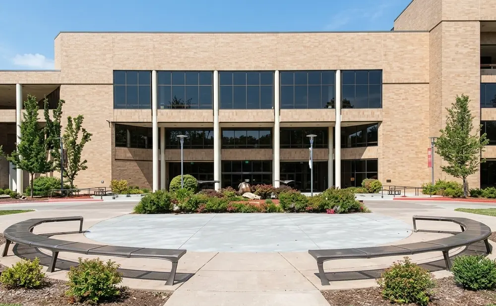 Modern brick building with large windows, curved benches, and manicured landscaping under a clear blue sky.