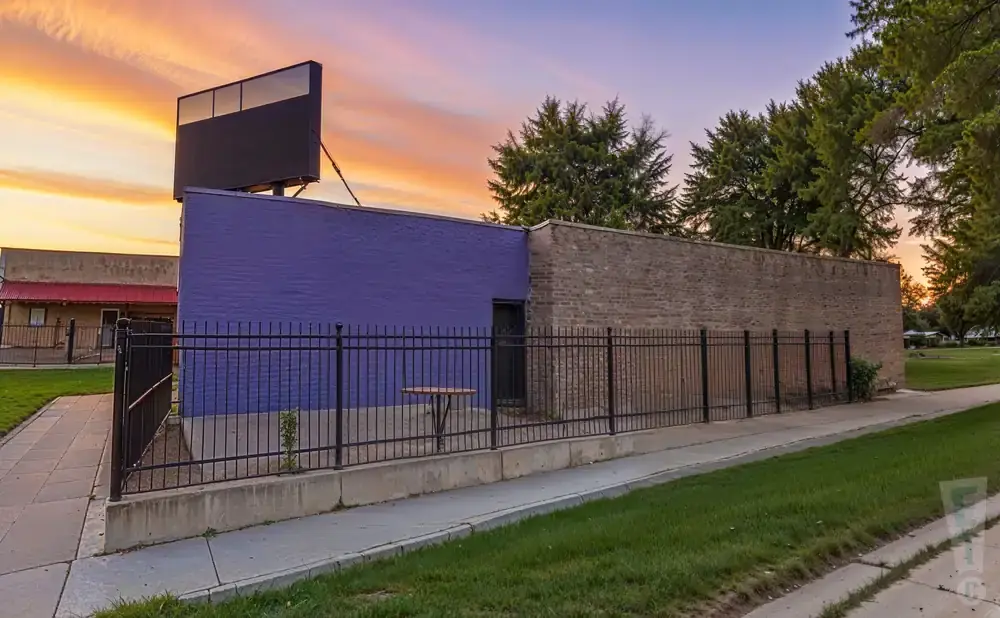 A purple and brick building with a large billboard against a colorful sunset sky.