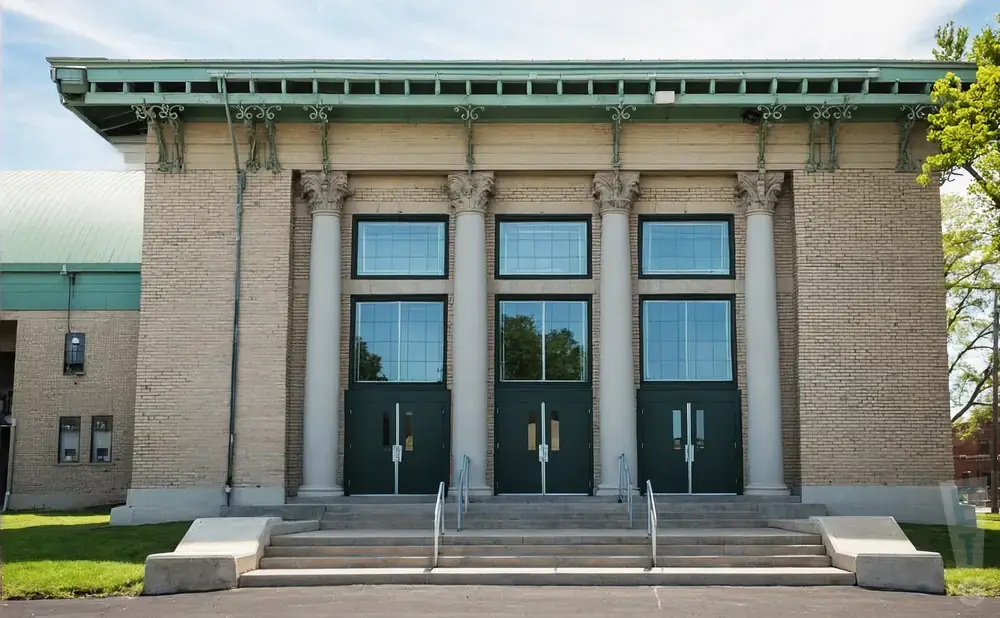 A beige brick building with three sets of double doors and three tall windows above each set, framed by columns and a green ornate roofline.