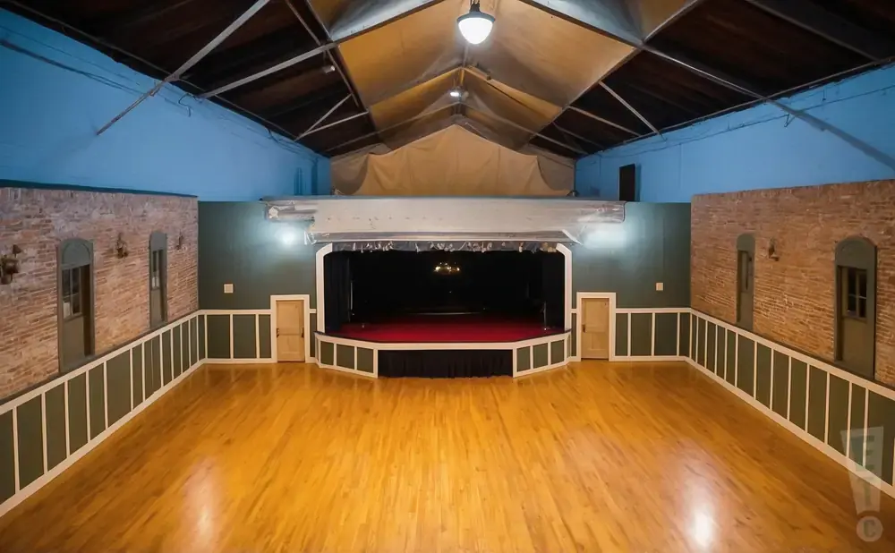 An empty ballroom with a stage, wooden floors, and exposed beams on the ceiling.