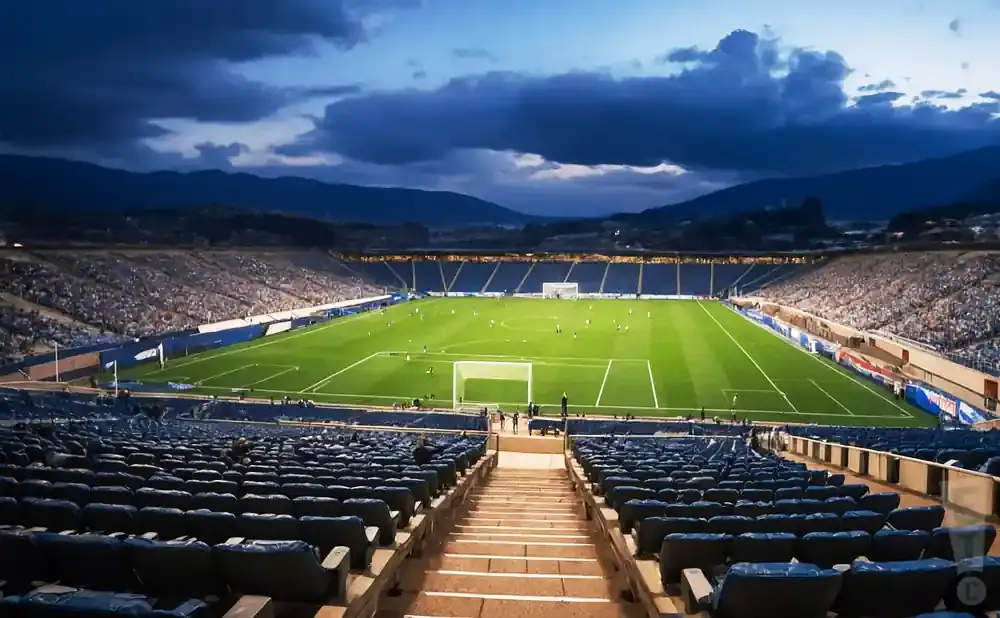 A soccer game at dusk in a stadium with mountain views.
