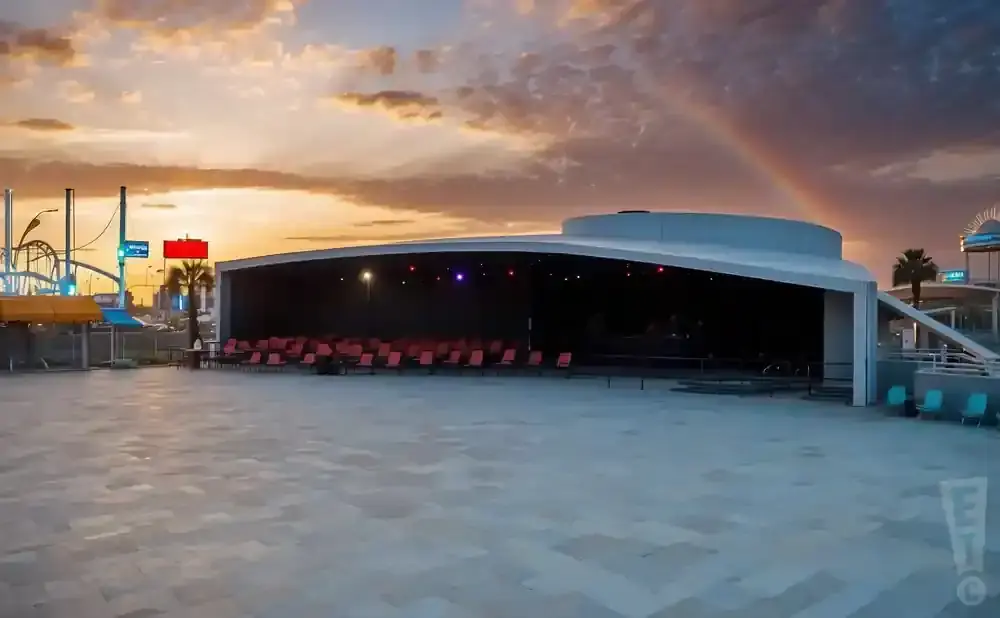 Outdoor amphitheater with rows of red seats under a rainbow at sunset.