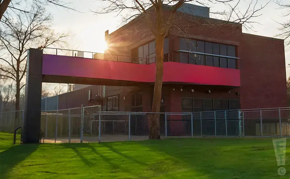 A modern brick building with a bright pink overhang and a chain-link fence in front.