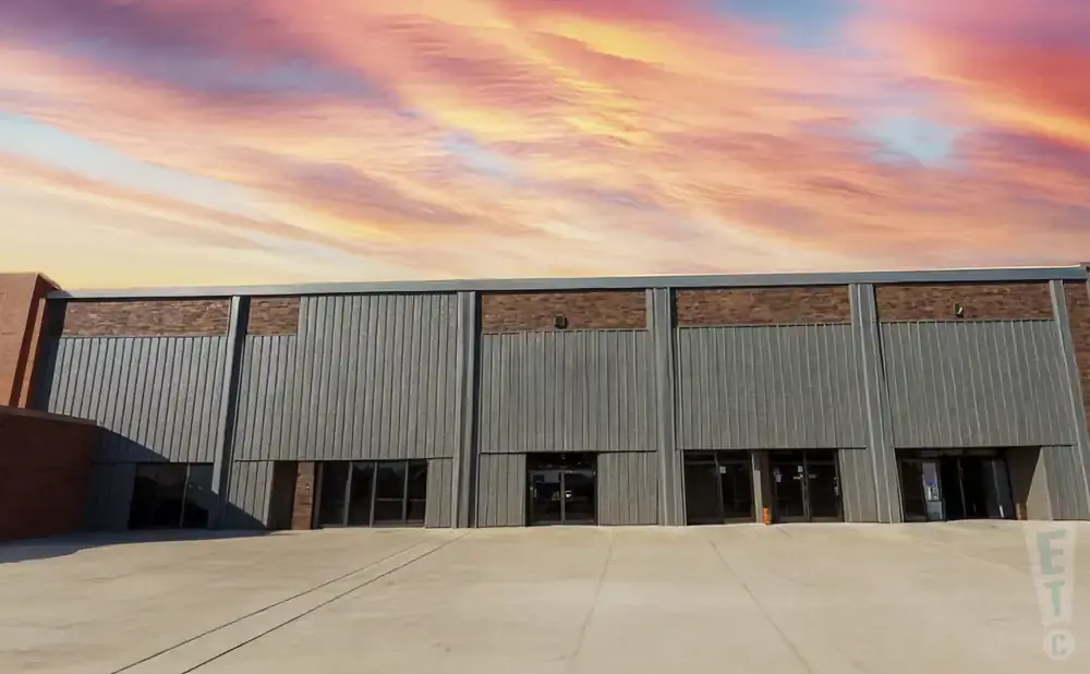 A modern industrial building with corrugated metal siding and a colorful sunset sky.