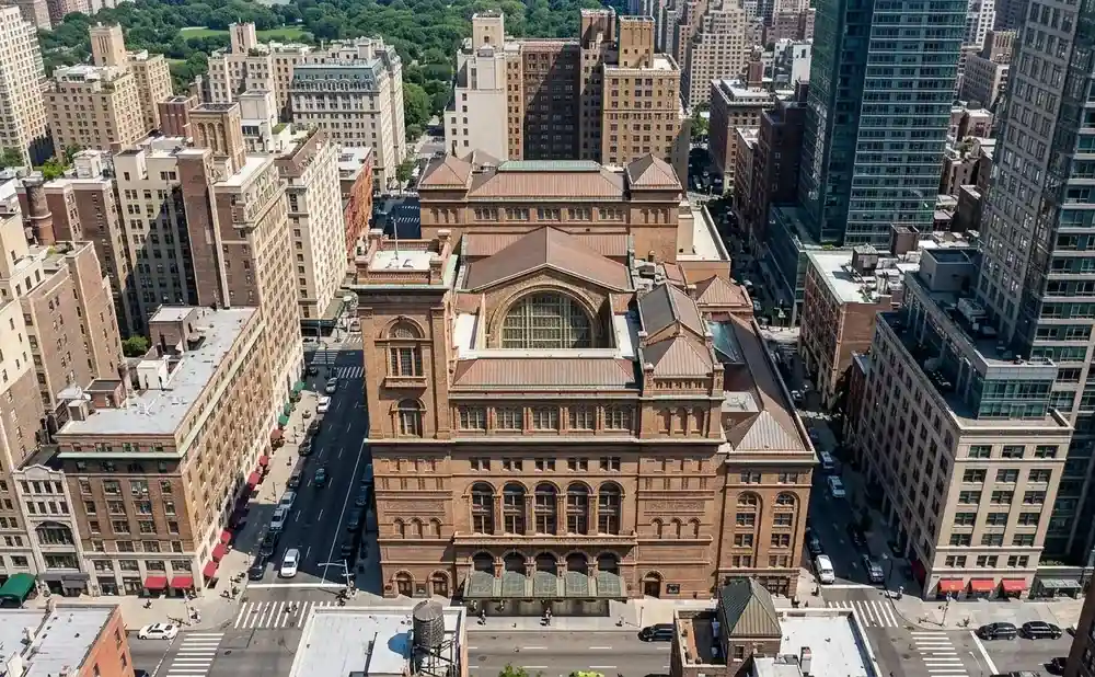 Aerial view of Carnegie Hall and surrounding Manhattan buildings, with trees and Central Park in the background.