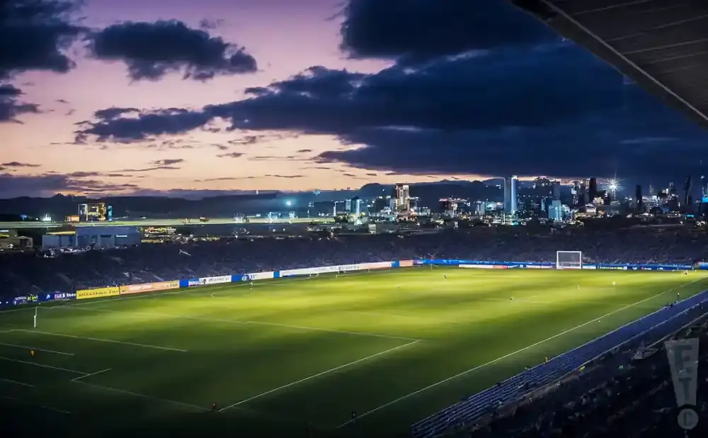 Soccer stadium at dusk with city skyline in background.