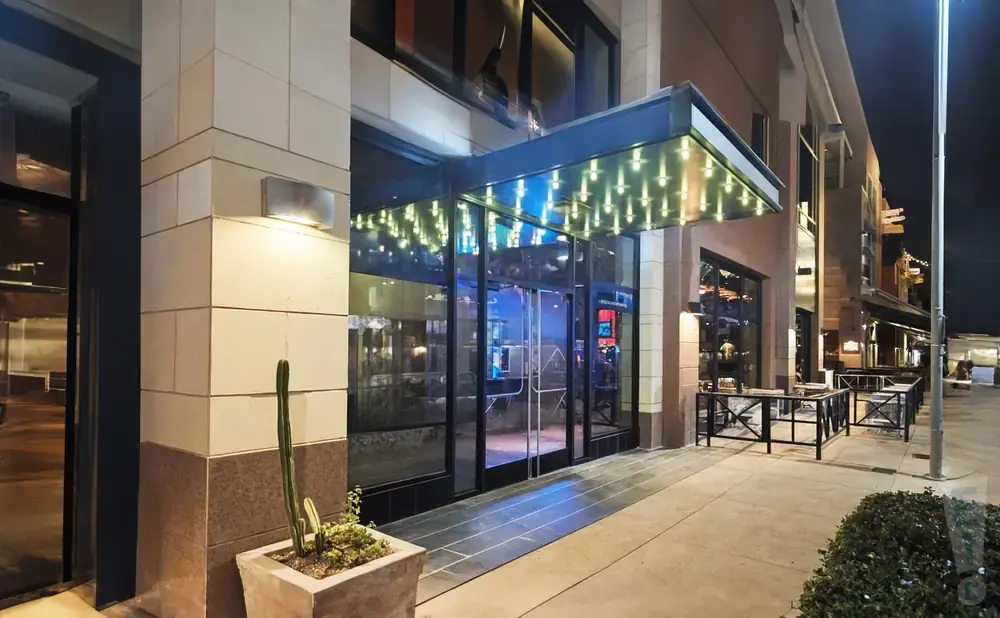 Exterior view of a modern building entrance at night with glass doors, exterior lights, and a potted cactus.