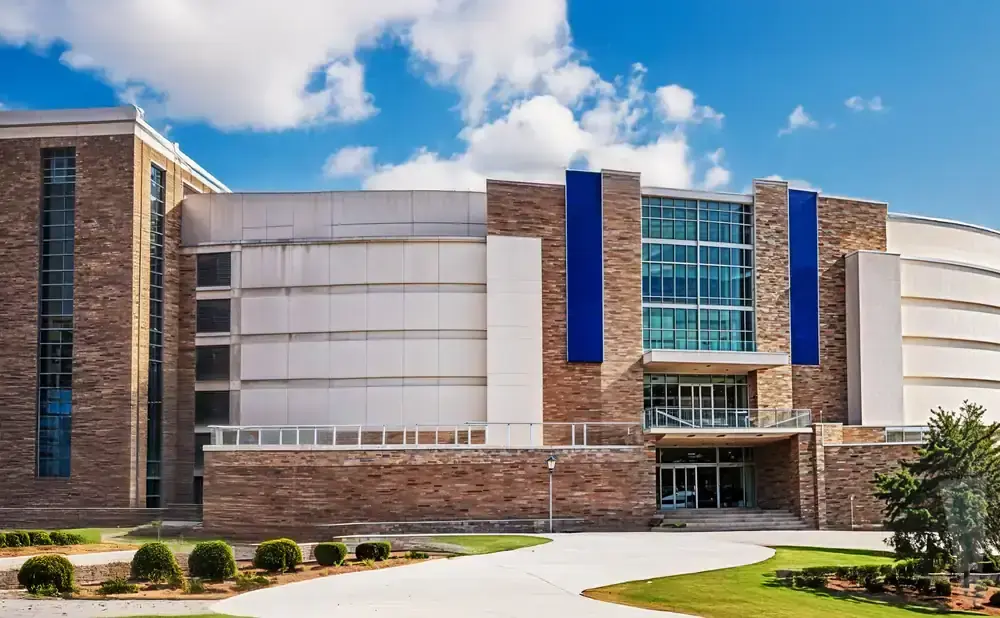 Modern building with brick and stone accents, featuring large windows and blue vertical panels, under a blue sky with clouds.