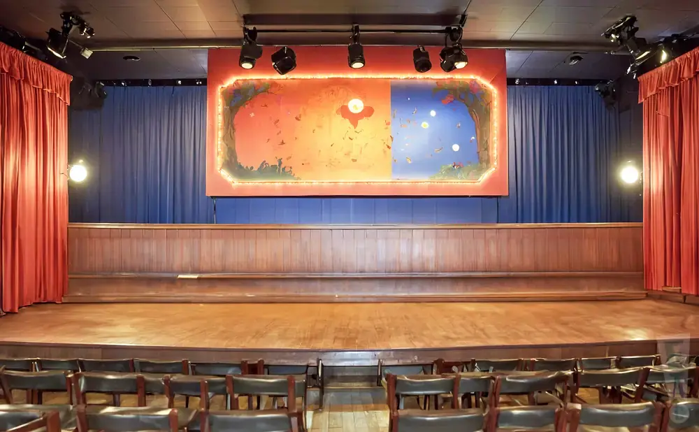 A stage with a mural, wooden seating, and red curtains.