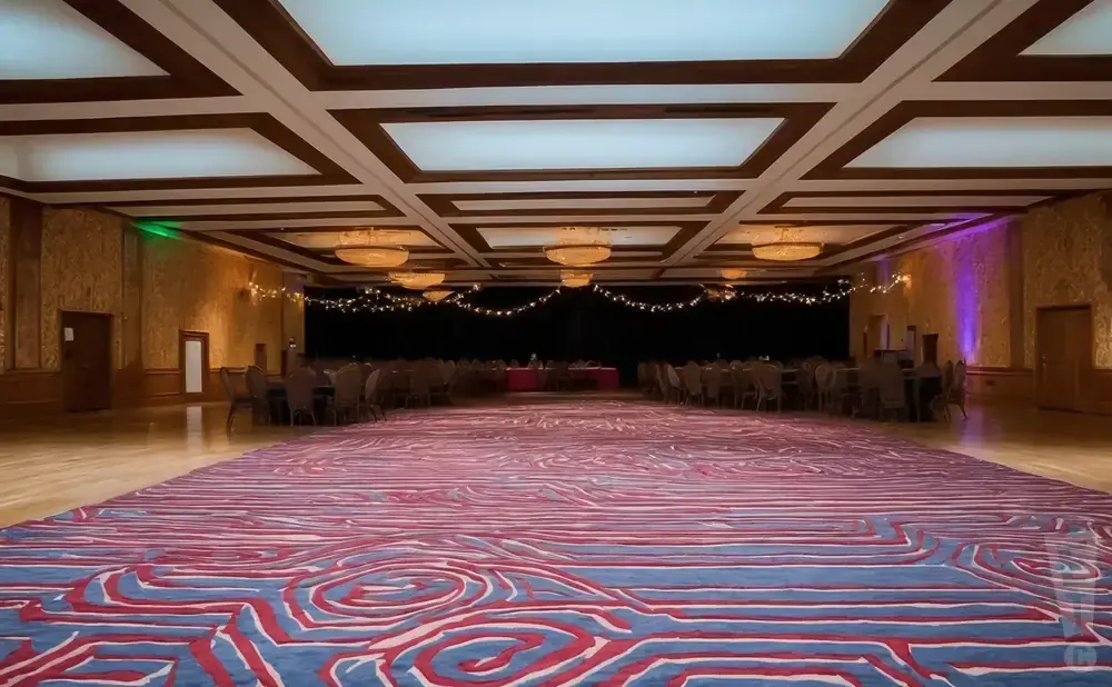 A grand ballroom with a red and blue patterned carpet, a coffered ceiling, and tables set up for an event.