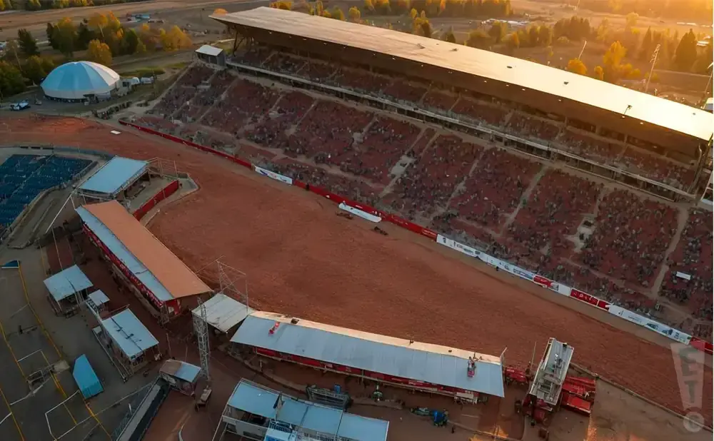 Aerial view of a rodeo arena with stadium seating and a large domed building.