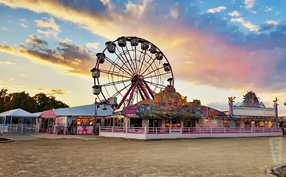 Ferris wheel and carnival rides at sunset with colorful clouds.