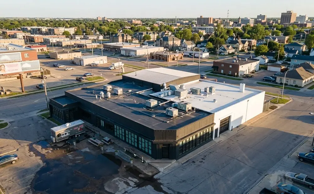 Aerial view of a dark-roofed building with large windows, a food truck, and a parking lot filled with cars.