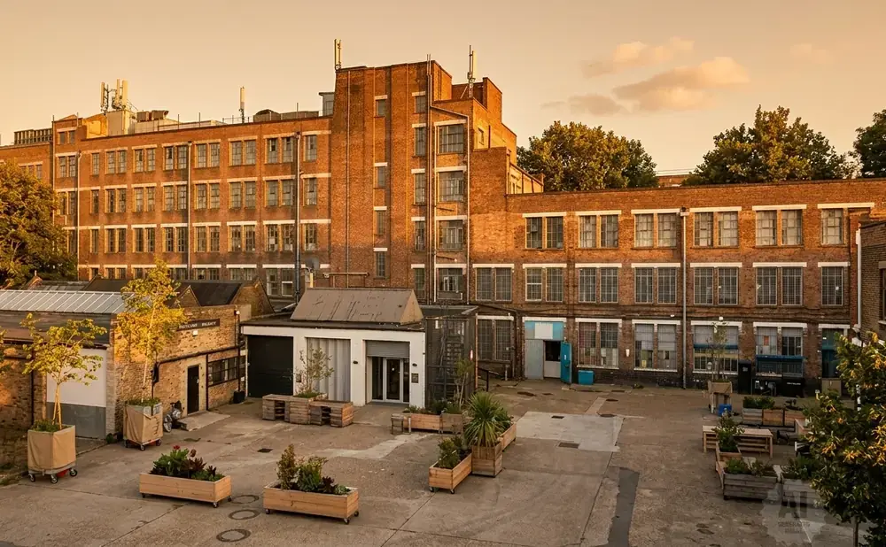 Courtyard of a brick industrial building with trees and outdoor seating.