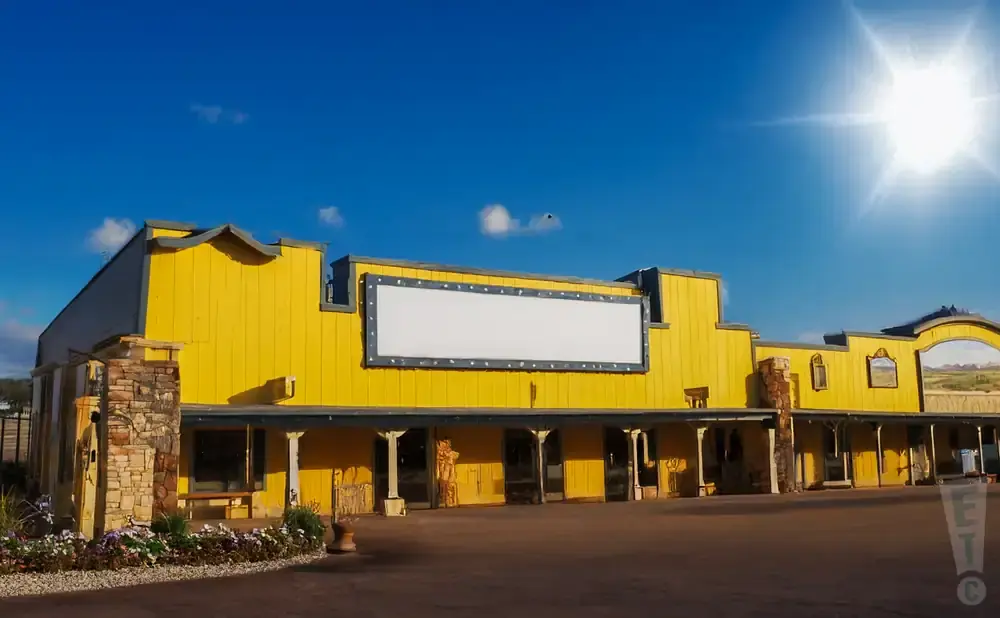 A bright yellow building with a large blank sign and a western mural under a sunny blue sky.