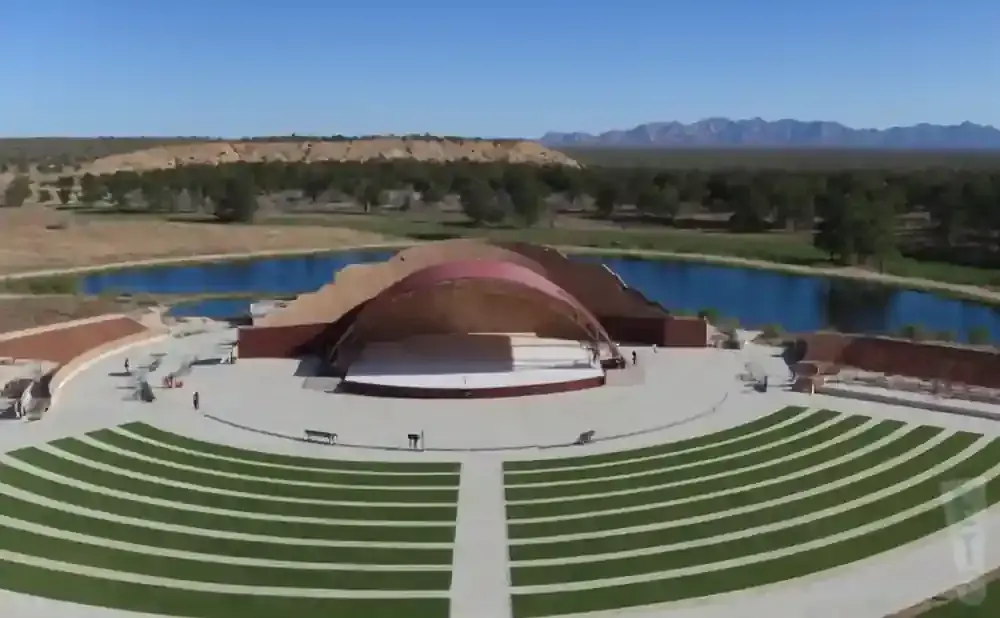 Outdoor amphitheater with a curved stage and seating, surrounded by water and arid landscape.