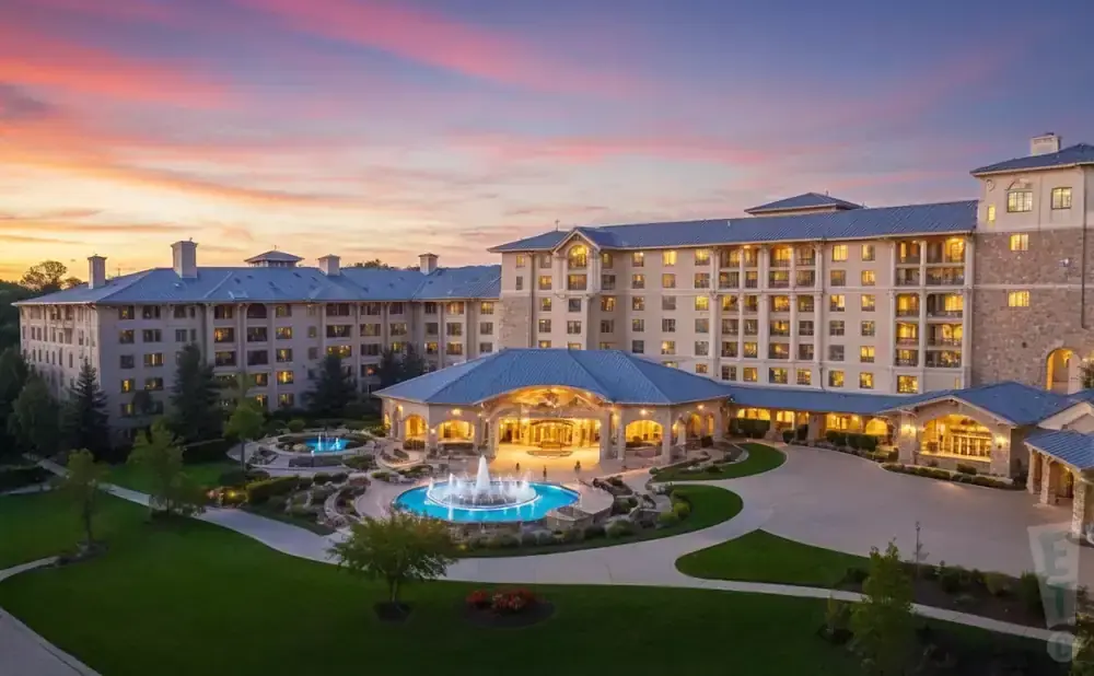 A large hotel complex with blue roofs and illuminated windows, set against a colorful sunset sky.