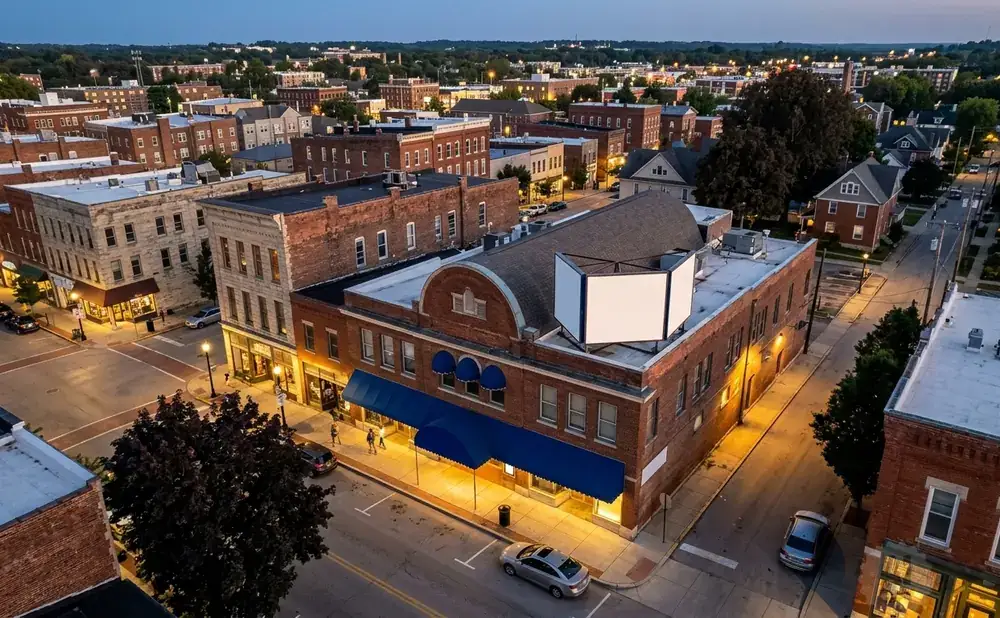 Aerial view of a charming town square with historic brick buildings, streetlights, and a few cars at dusk.