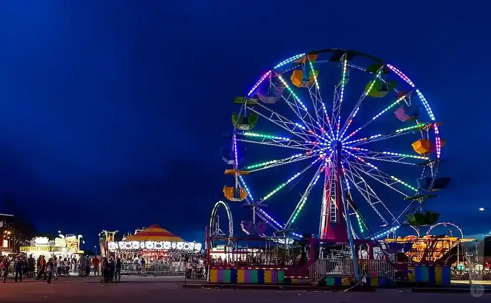 A brightly lit Ferris wheel and carousel at a carnival at dusk.